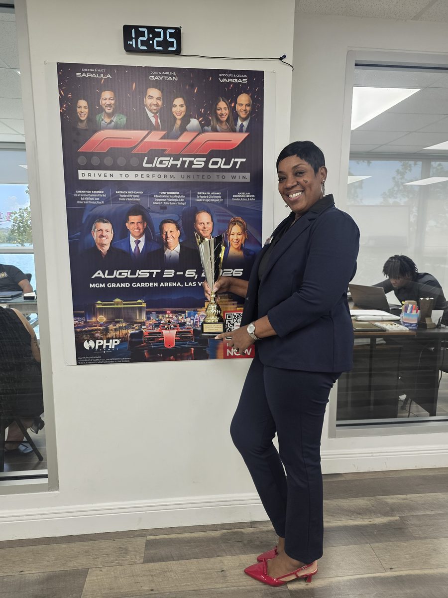 A BTT team member with the Lights Out Champion trophy beside the PHP Lights Out event poster in the office