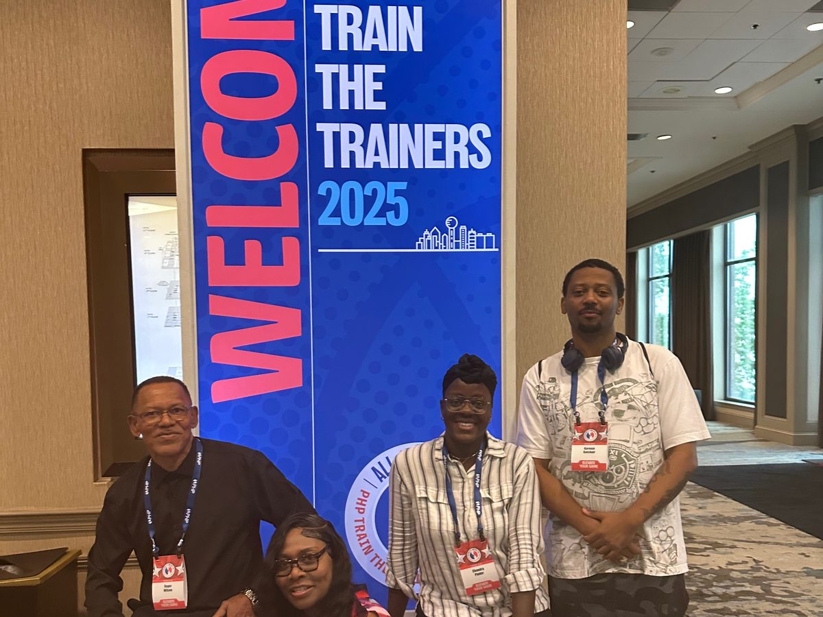 Four BTT team members at the PHP Train the Trainers 2025 welcome banner